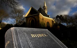 Op de voorgrond een Bijbel, op de achtergrond een verlicht kerkje tegen de avondhemel.