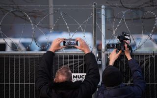Twee mannen houden hun camera’s boven een hek. 