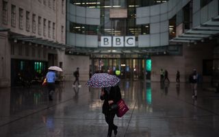 Een vrouw loopt onder een paraplu voor een kantoorgebouw. 