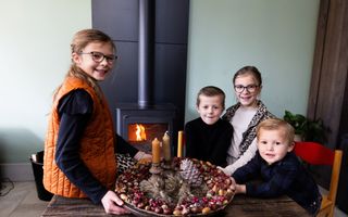 Vier kinderen poseren met een krans gemaakt van kastanjes, eikels en sneeuwbessen op een schaal.