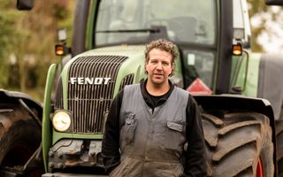 Man in overall staat voor zijn groene trekker van het merk Fendt. 