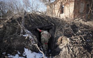 Een soldaat in uniform kijkt in een verlaten schuilplaats die is bedekt door takken.