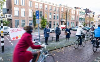 Vrouwen staan op de stoep langs een fietspad met flyers in de hand. 