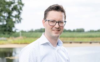 Jonge man in overhemd met bril staat in een natuurrijke omgeving.