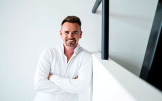 Jonge man in wit overhemd staat tegen een witte muur.