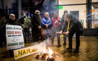 Man warmt handen boven vuurtje dat zich twee voor protestborden bevindt. Op de achtergrond meer mensen.