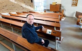 Man in trui, zittend in een kerkbank. Rechts van hem een bedieningspaneeltje voor licht en geluid. Voorin de houten preekstoel.