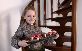 Meisje met langwerpige schaal vol paddenstoelen van klei, mos en andere herfstproducten.