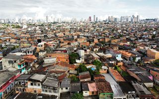 Een luchtfoto van een wijk vol krakkemikkige huisjes. In de verte de hoogbouw van Belém.