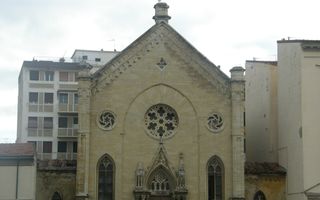 Oud kerkgebouw, ingeklemd tussen appartementencomplexen. Op de voorgrond geparkeerde auto’s.