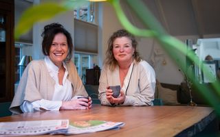 Donkere en blonde vrouw zitten samen aan tafel.