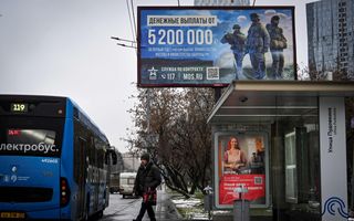 Een man staat bij een bushokje. Boven het bushokje staat een billboard.