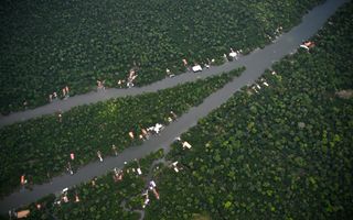 Luchtfoto met rivieren, bomen en paalwoningen langs de rivier.