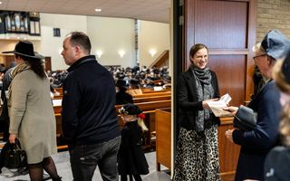 Een vrouw deelt programmaboekjes uit aan mensen die een kerkzaal binnenlopen.