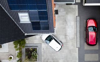 Luchtfoto van zonnepanelen op het dak van een woning, waarnaast twee auto’s staan.