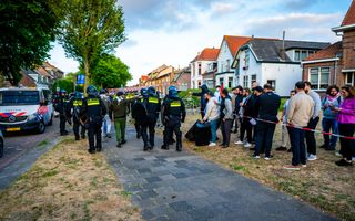 Mensen achter een lint. Daarnaast met schilden bewapende politiemensen.