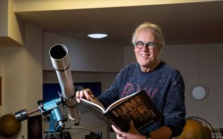 Man bladerend in een boek naast een telescoop.