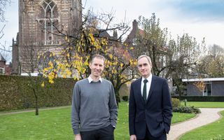 Erik-Jan Verbruggen in grijze trui en Laurens van der Tang in zwart pak staan in een tuin, met op de achtergrond een oude kerktoren.