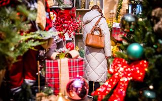 Dame met lange grijze jas in een winkel met kerstversieringen.