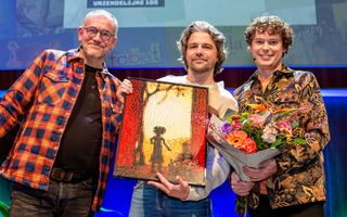 Drie mannen staan naast elkaar, de middelste houdt een schilderij omhoog dat is gemaakt met legosteentjes. De rechter houdt een bos bloemen vast