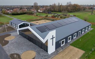 Het nieuwe kerkbouw, met een groot kruis. Het gebouw ligt tussen de weilanden.