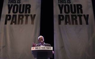 Man met grijs haar en een bril staat achter een spreekgestoelte, met daarop de tekst ”This is your party”. 