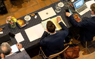 Een foto van een tafel van bovenaf waarop mensen bezig zijn met hun laptop en tablet.