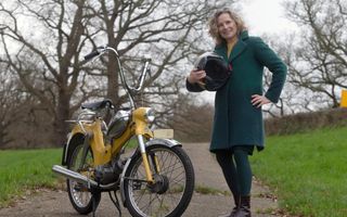 Vrouw met helm in haar hand bij haar gele Puch.