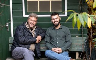 Twee mannen zitten op een houten bank voor een tuinhuis.