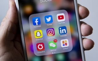 Een hand houdt een smartphone vast met daarop de apps Facebook, Twitter (nu X), YouTube, Snapchat, Instagram, LinkedIn, Crowdfire, WeChat en Collect.
