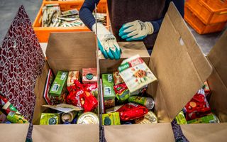 Twee handen met handschoenen stoppen een product in een door met levensmiddelen.