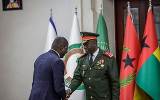 Kale man in blauw streepjespak schudt de hand van een man in groen uniform.