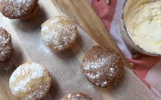 Kleine cakejes op een houten plank met een vel bakpapier. Rechts een schaal room.