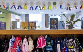 Rijen gekleurde rugtassen hangen aan een kapstok.