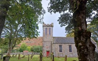 Kerkje met rode deur en vierkante toren grenst aan een begraafplaats met gras.