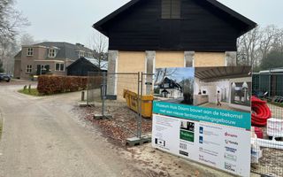 Bord van de aannemer op bouwhek voor gebouw dat met hout tijdelijk afgesloten is.