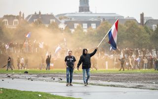 Een man zwaait met een Nederlandse vlag op een vlaggenstok, met op de achtergrond andere demonstranten met vlaggen en spandoeken.