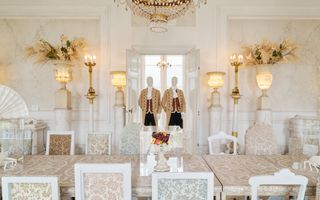 Twee lakeien in de deuropening. Fruit onder een glazen stolp. Bloemstukken boven brandende lampen.