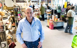 Man in een blauwe spijkerbroek en een lichtblauw overhemd, met daarachter een winkelinterieur. Daar zijn onder meer kassa’s te zien.