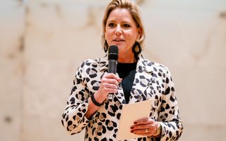 Blonde vrouw van middelbare leeftijd met microfoon in haar hand.