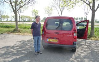 Man in blauwe shirt bij rode bestelauto.