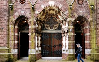 Een man met een baseballpetje op loopt langs openstaande kerkdeuren.