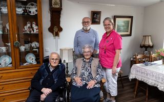 Twee oude mensen zitten in een stoel. Een jongere man en een vrouw staan schuin achter hen. 