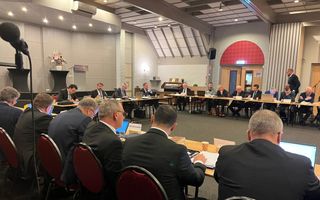 U-vormige vergadertafel, met daar omheen tientallen mannen in donkere pakken.