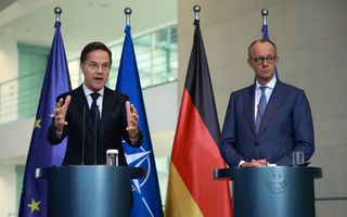 Twee heren in formele kleding achter spreekgestoelte. Achter hen vlaggen van Europa. de NAVO en Duitsland