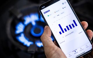 Een overzicht op het scherm van een martphone van het energieverbruik van een huishouden, met op de achtergrond een brandend gasfornuis.
