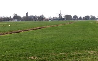 Groene weilanden, doorsneden door sloten. Op de achtergrond een dorp met een kerk en een molen.