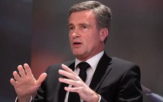 Man in zwart pak, met gestreepte stropdas. Hij houdt zijn handen in een gebaar.