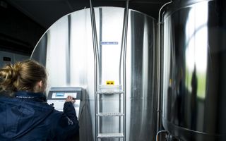 Een jonge vrouw toetst iets in op een scherm, dat aan een grote grijze tank hangt.