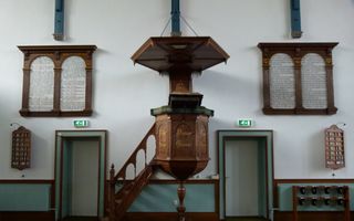 Houten preekstoel met daarnaast deuren, met aan de muur onder andere psalmborden. 